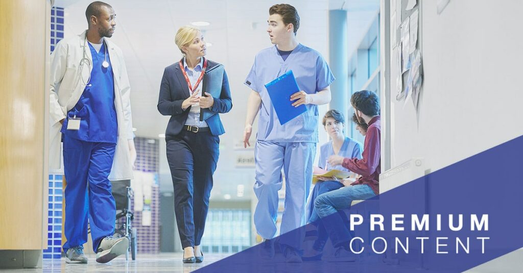 A mid adult male doctor speaks with a businesswoman, sales person on the hospital corridor as they head to a meeting, with a young female nurse and patients in the busy corridor.