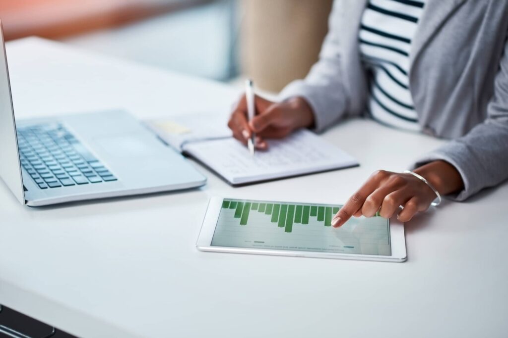 Writing notes from looking at a tablet and laptop on a desk