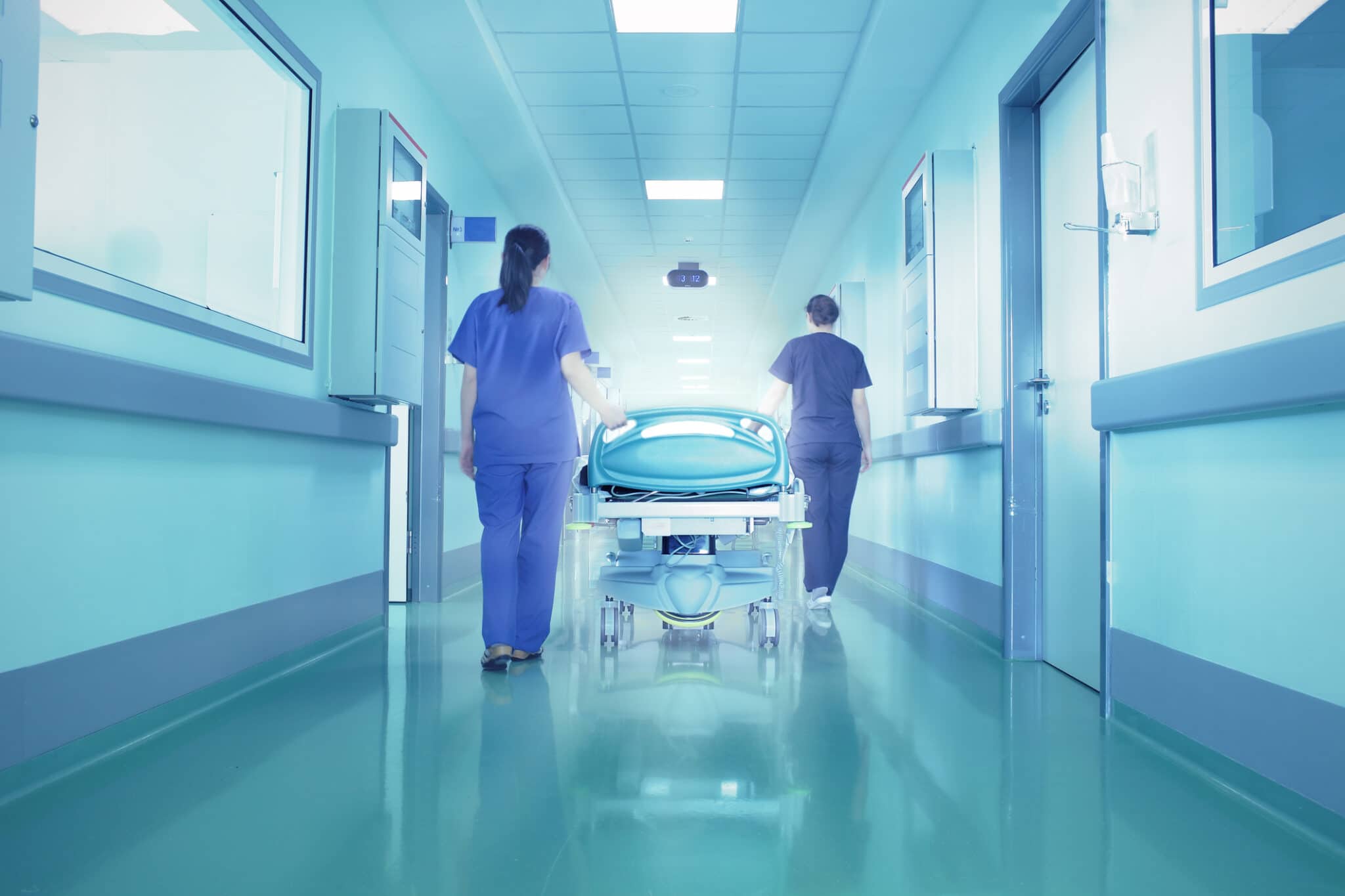 Nurses walking hospital bed through hallway