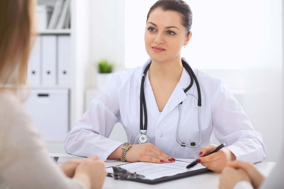 Brunette female doctor talking to patient in the hospital office.