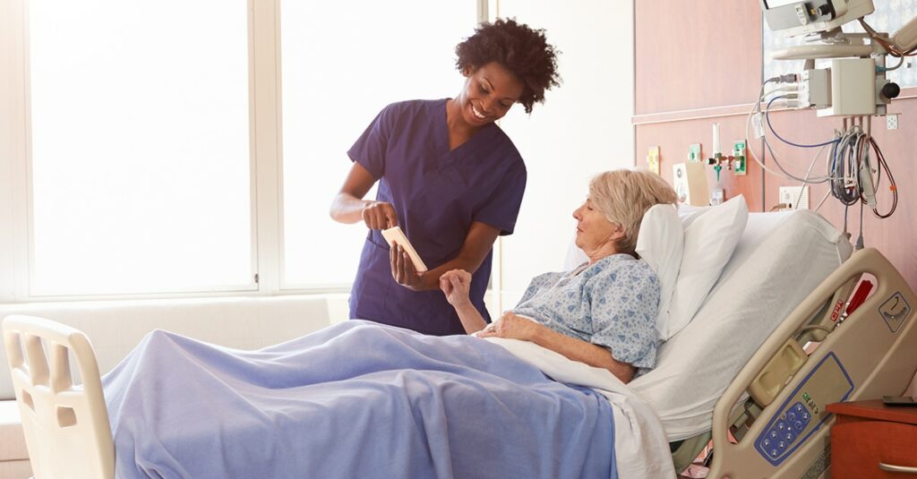 Hospital Nurse With Digital Tablet Talks To Senior Patient